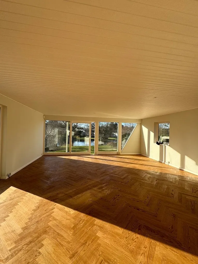 Stort rum med sildebensparket og panoramavinduer mod haven